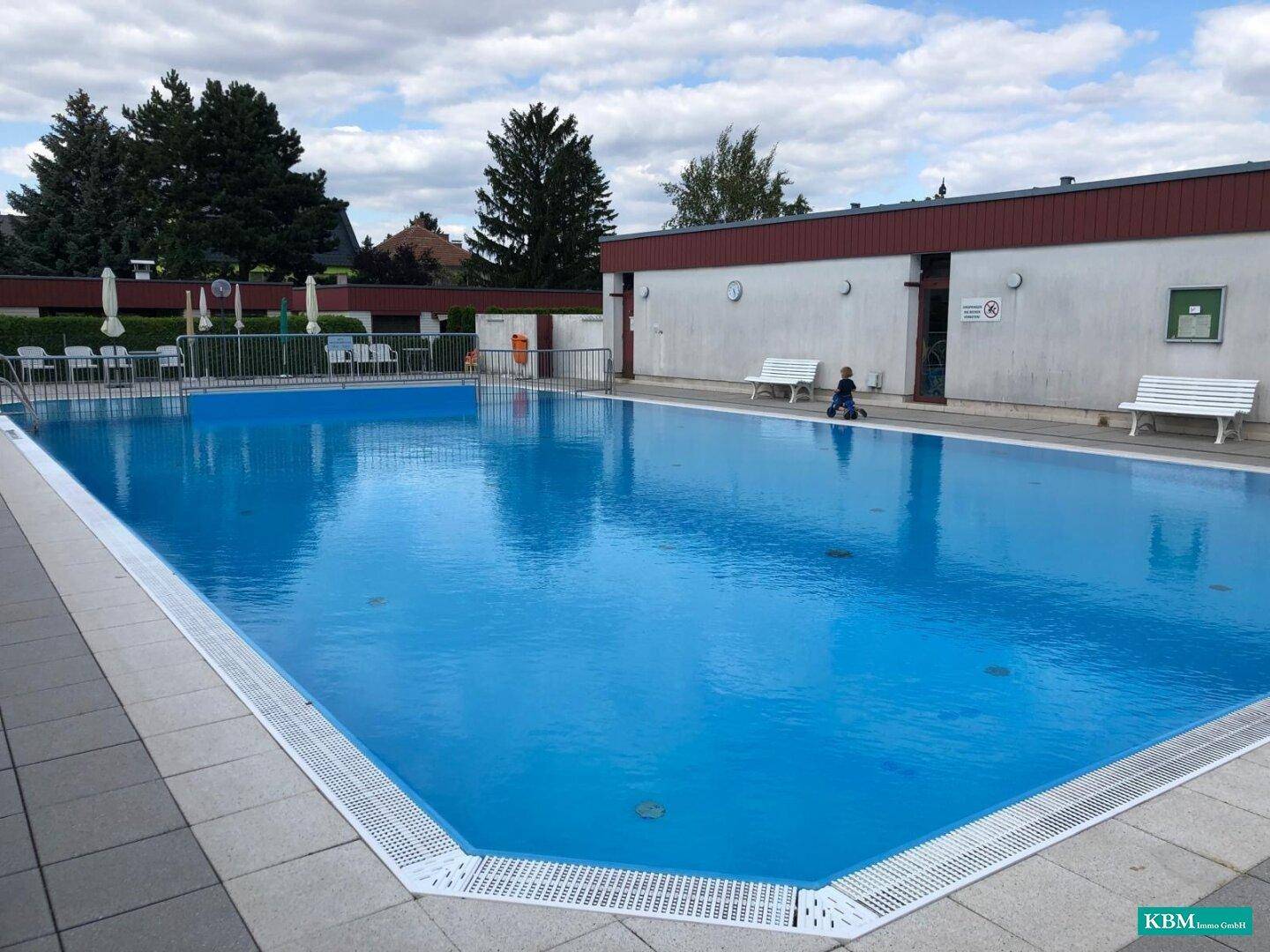Großer Außenpool mit klarem Wasser, Liegebereich und umliegenden Gebäuden.