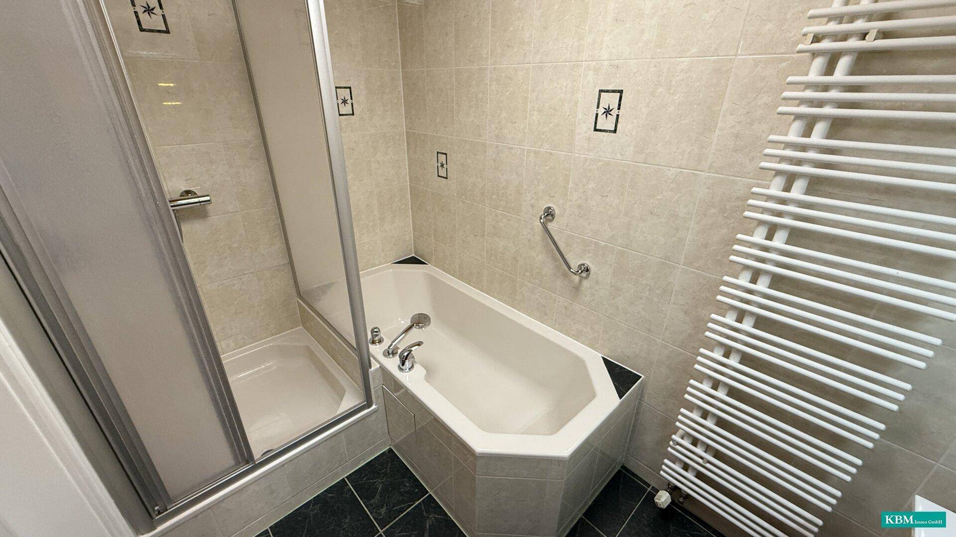 Badezimmer mit Duschkabine, Eckbadewanne, Handtuchheizkörper und beigen Wandfliesen.