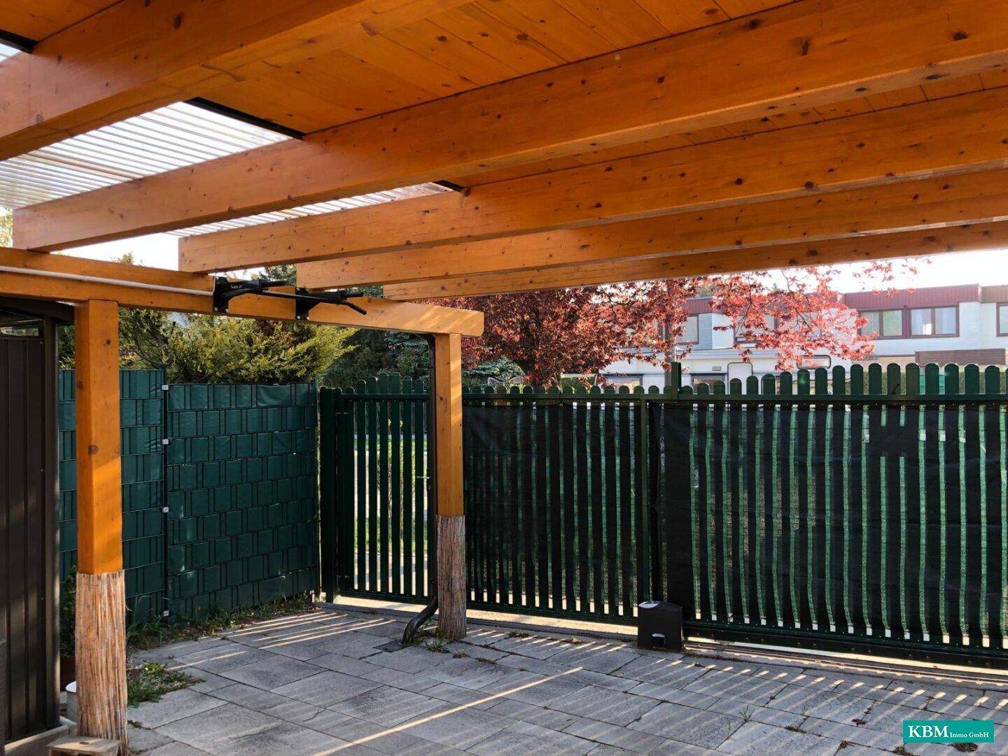 Geräumiges Holzcarport mit robusten Holzbalken und einer gepflasterten Einfahrt, umgeben von einem Zaun.