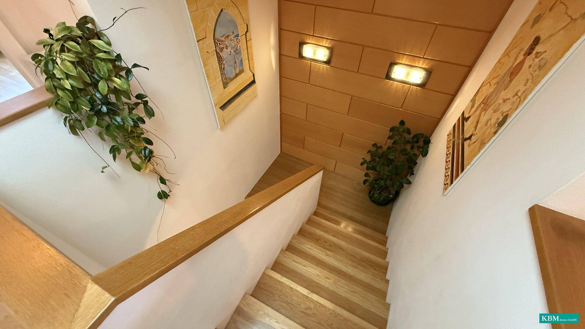 Treppenhaus mit Holzstufen, hellem Geländer und dekorativen Wandelementen.