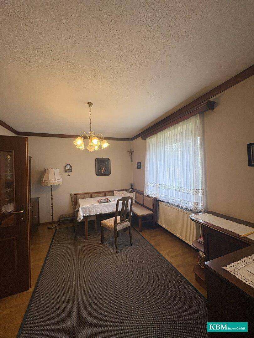 Esszimmer mit Holzbänken, Esstisch und Teppichboden, gut beleuchtet durch ein Fenster.