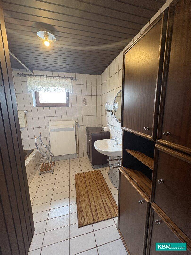 Badezimmer mit weißen Fliesen, Holzschränken und Fenster, ausgestattet mit Badewanne.