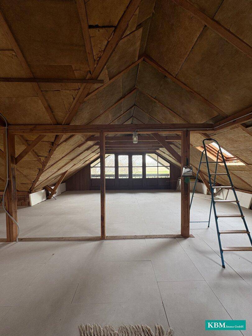 Ausbaufähiger Dachboden mit sichtbaren Holzbalken und Dachfenstern.