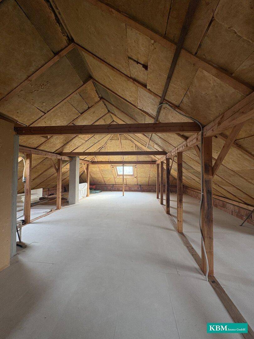 Geräumiger Dachboden mit Isolierung und Holzbalken, bereit für den Ausbau.