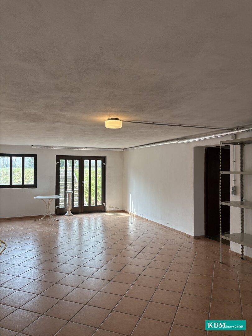 Heller Kellerraum mit Fliesenboden und Zugang zum Garten durch eine Tür.