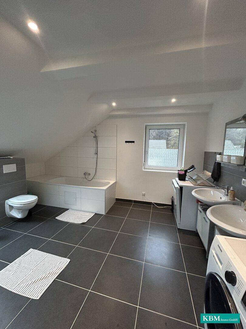 Geräumiges Badezimmer mit Badewanne, Doppelwaschbecken und Dachschräge.
