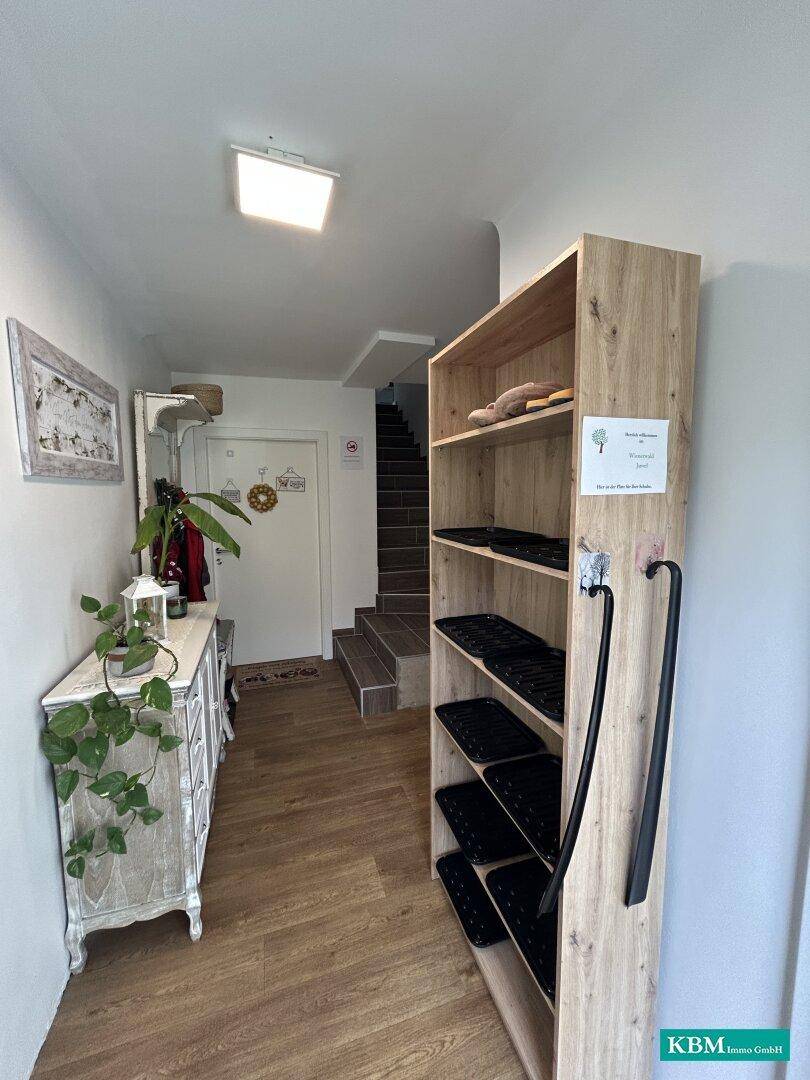 Eingangsbereich mit Holzoptik-Boden, Schuhregal und Treppe zum Obergeschoss.