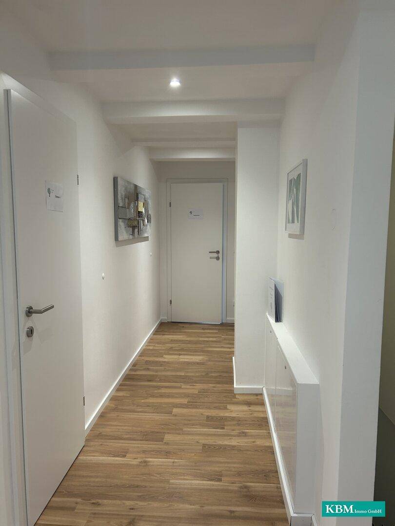 Heller Flur mit Holzoptik-Boden, weißen Wänden und modernen Dekorationselementen.