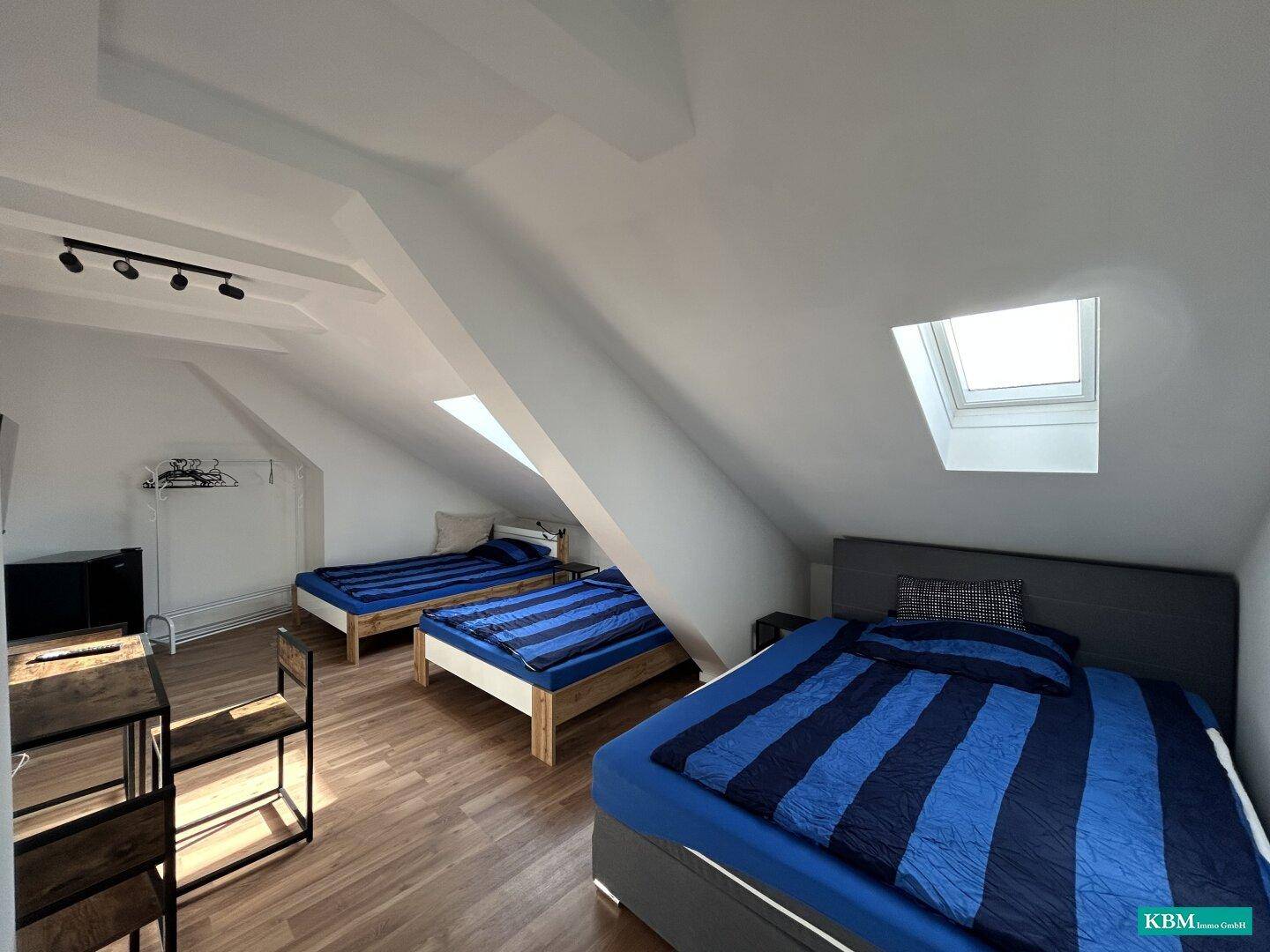 Geräumiges Schlafzimmer im Dachgeschoss mit mehreren Betten, Dachschrägen und Dachfenster.
