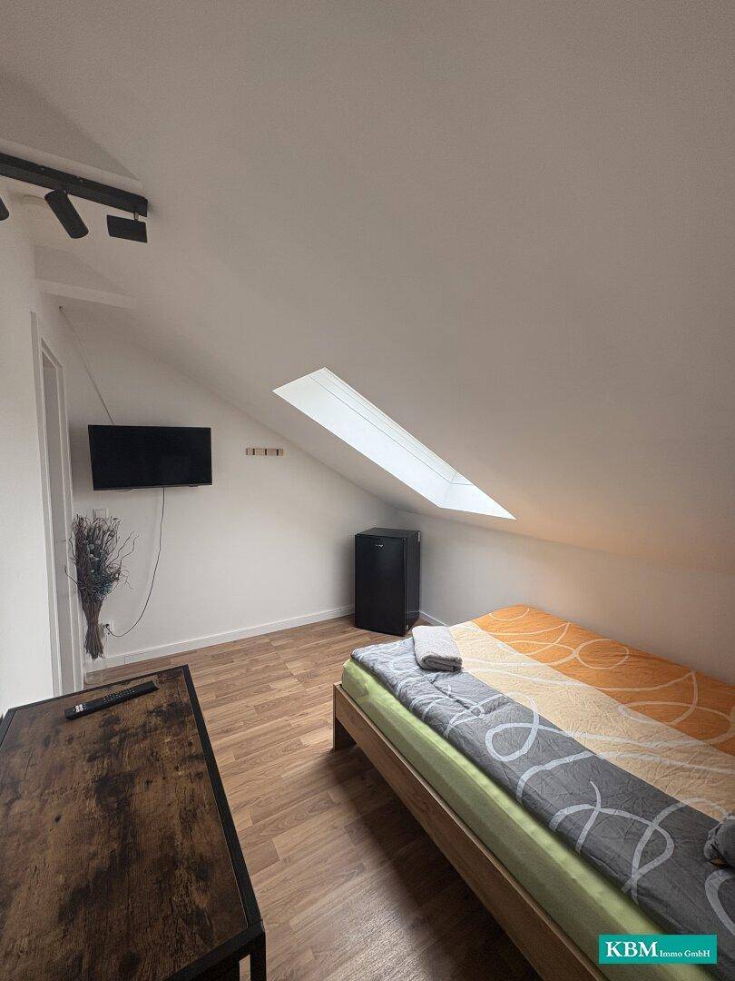 Einzelzimmer im Dachgeschoss mit Bett, Fernseher, Minikühlschrank und Dachschräge.