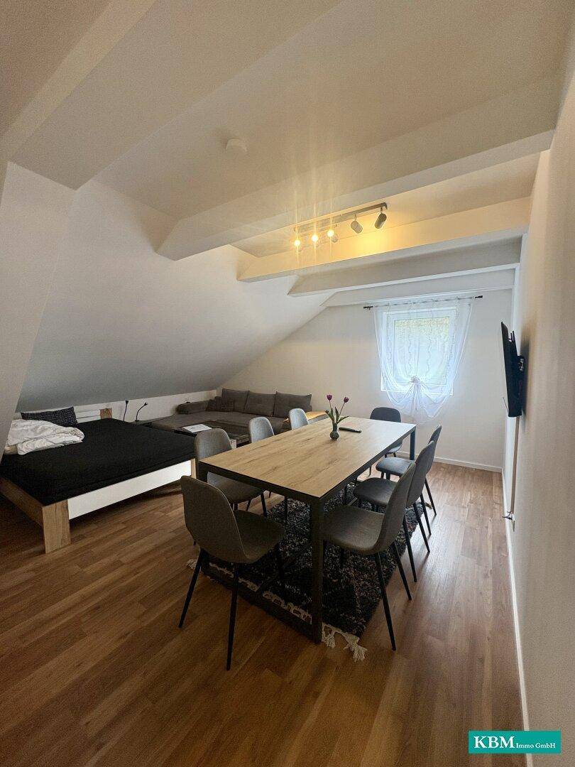 Kombinierter Wohn- und Essbereich im Dachgeschoss mit Esstisch, Sofa und Bett.