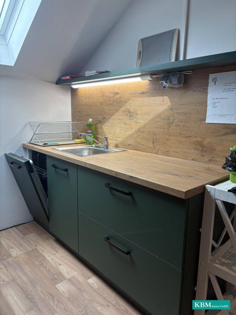 Moderne Küchenzeile im Dachgeschoss mit grünen Schränken, Holzoptik-Arbeitsplatte und Dachfenster.