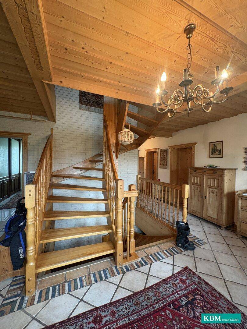Geräumiger Flur mit Holztreppe, Holzbalkendecke und traditionellem Teppich auf Kachelboden.