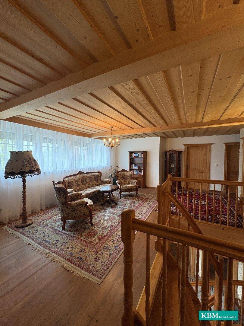 Helles Wohnzimmer mit Holzbalkendecke, traditionellen Möbeln und großen Fenstern mit Vorhängen.