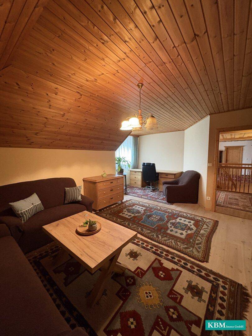 Gemütliches Zimmer im Dachgeschoss mit Holzverkleidung, Teppichen und einem Arbeitsbereich.