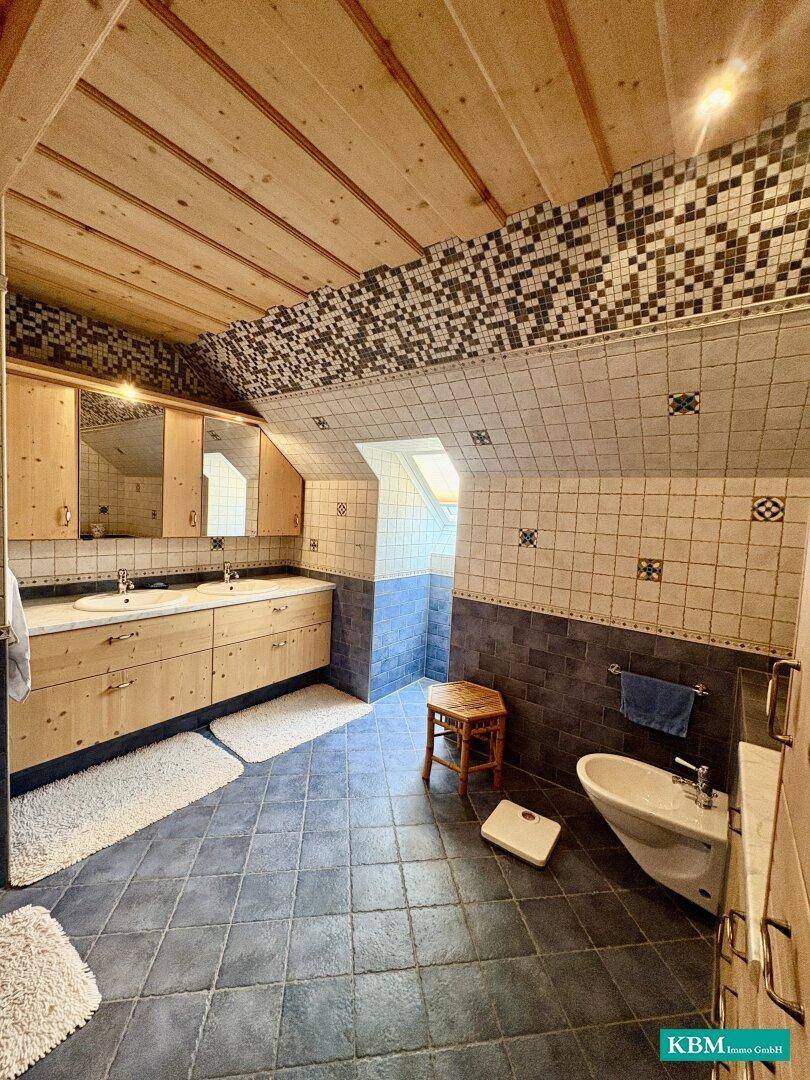 Badezimmer im Dachgeschoss mit Doppelwaschbecken, Bidet und gemusterten Fliesen an Wänden und Boden.