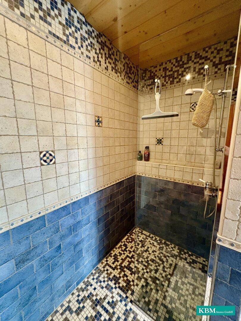 Duschbereich im Badezimmer mit blauen und weißen Mosaikfliesen und moderner Duscharmatur.