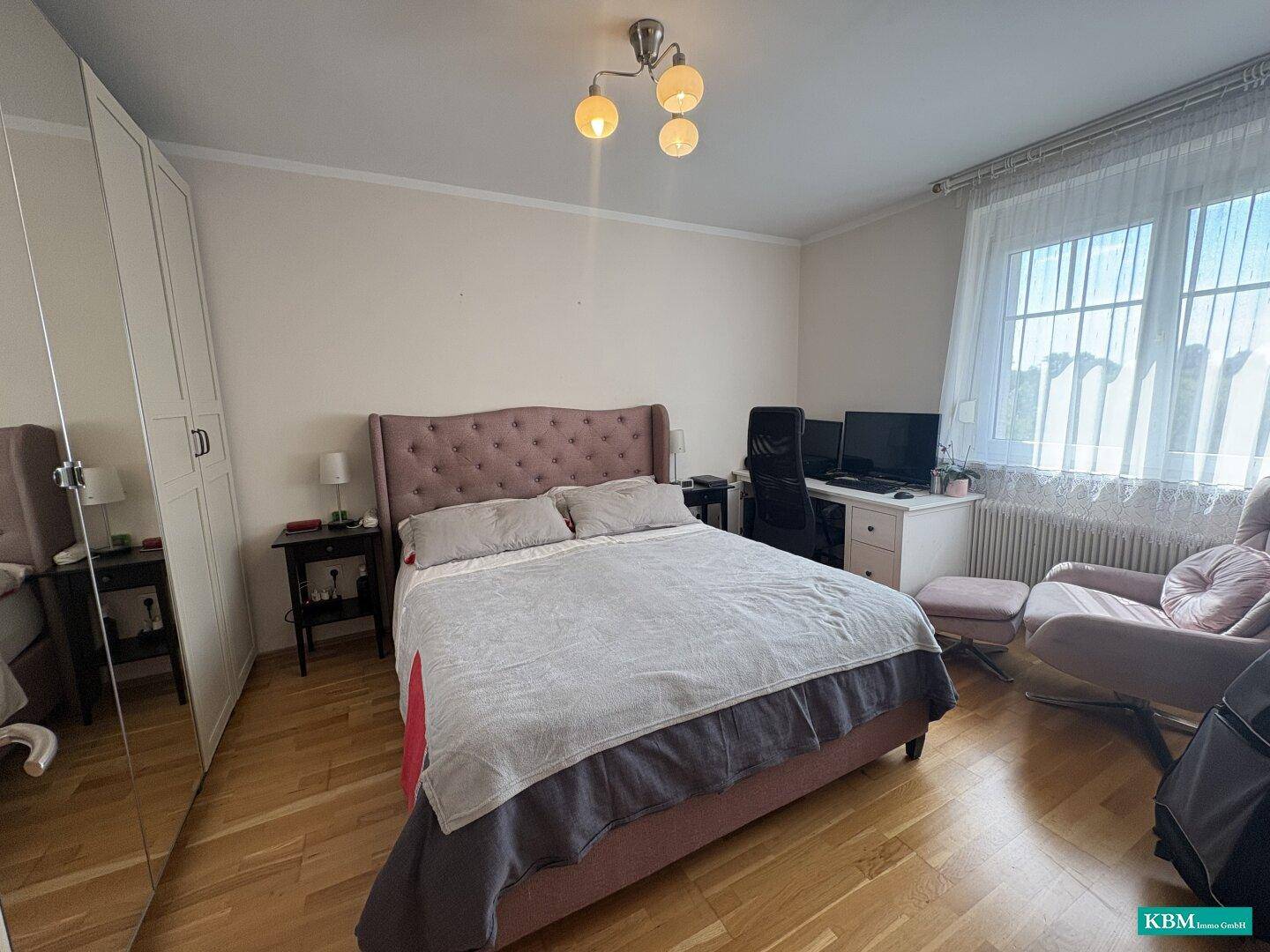 Helles Schlafzimmer mit Holzboden, großem Bett, Spiegelschrank und Schreibtisch am Fenster.