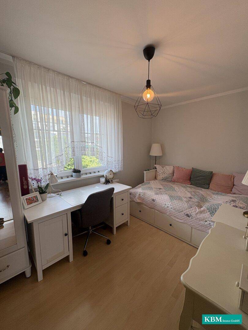 Freundliches Schlafzimmer mit Einzelbett, Schreibtisch am Fenster und hellem Holzboden.