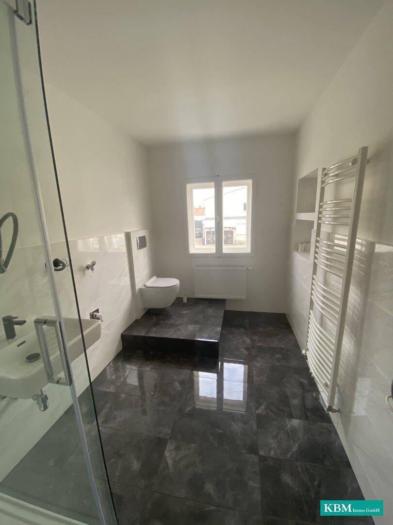 Helles Badezimmer mit Duschkabine, WC, beheiztem Handtuchhalter und Fenster für frische Luft.