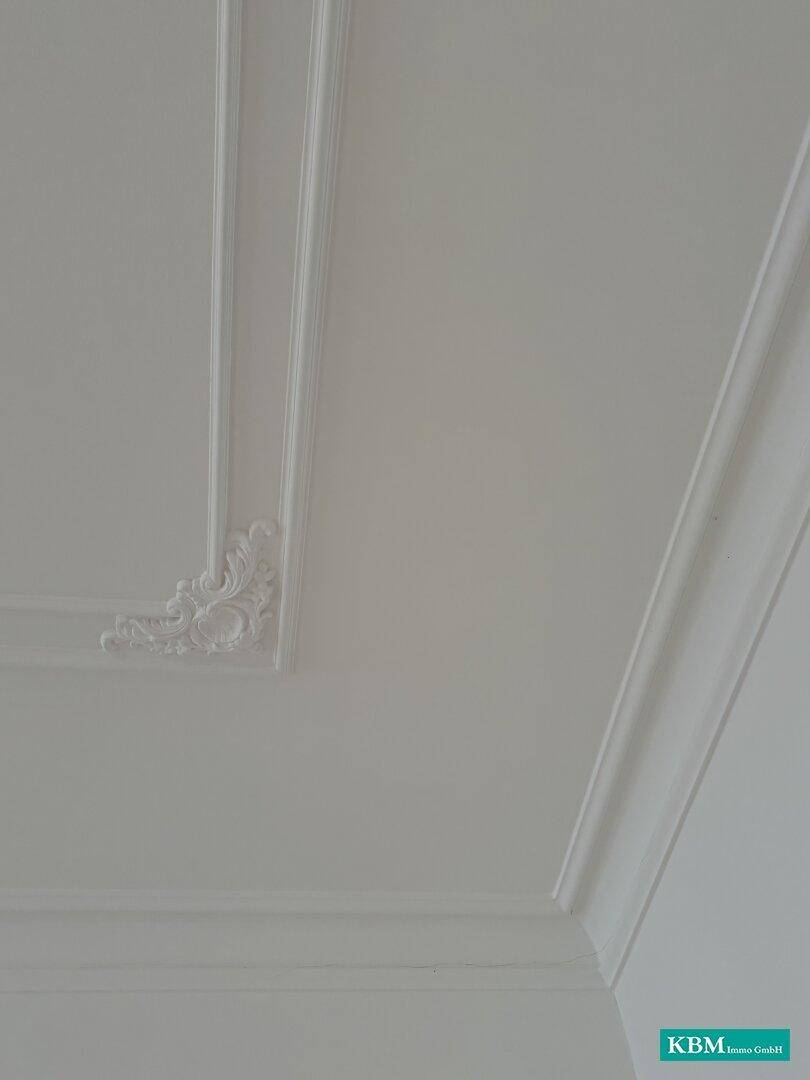 Detailaufnahme einer weißen Decke mit klassischer Stuckverzierung und Zierleisten.