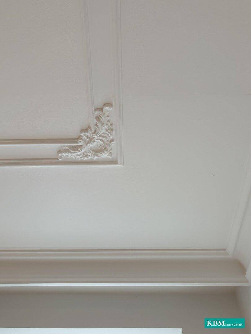 Nahaufnahme einer weißen Decke mit eleganter Stuckverzierung und feinen Details.