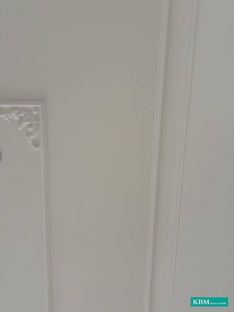 Ausschnitt einer weißen Decke mit schlichter Stuckverzierung und klaren Linien.