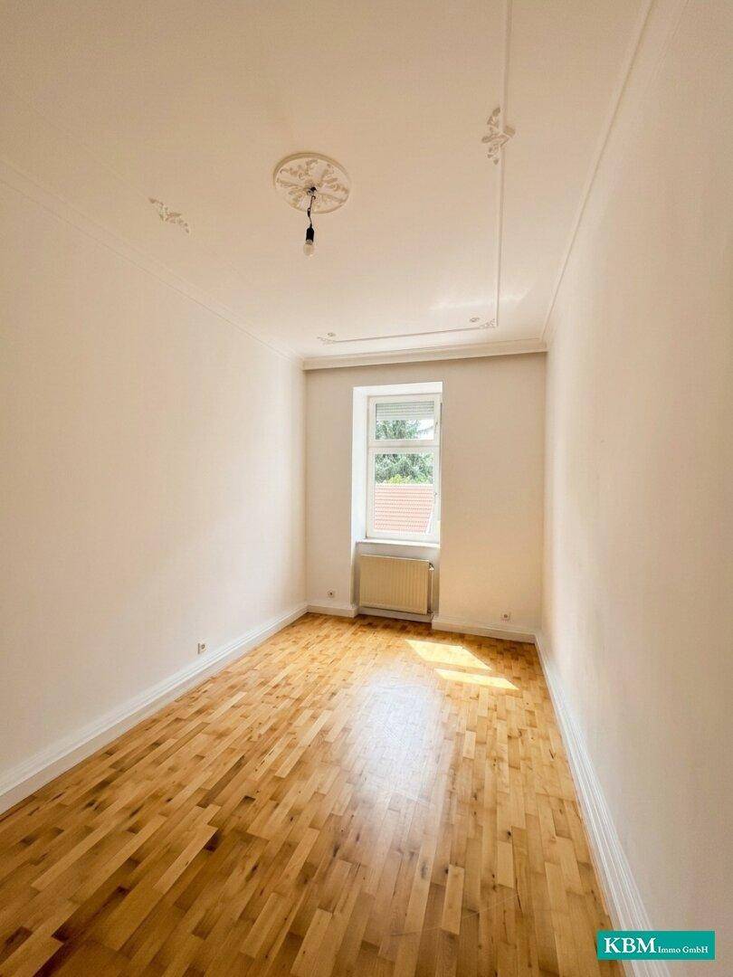 Gemütliches Schlafzimmer mit Holzboden, einem Fenster und Stuckelementen an der Decke.