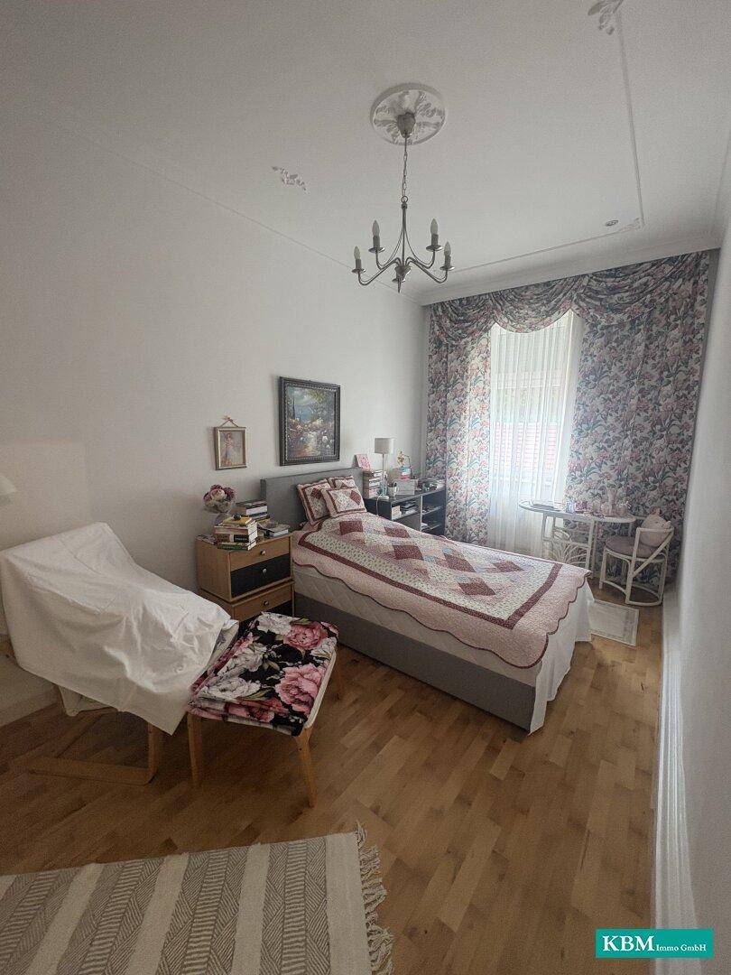 Schlafzimmer mit Holzboden, Einzelbett und floralen Vorhängen, bereit zur Einrichtung.