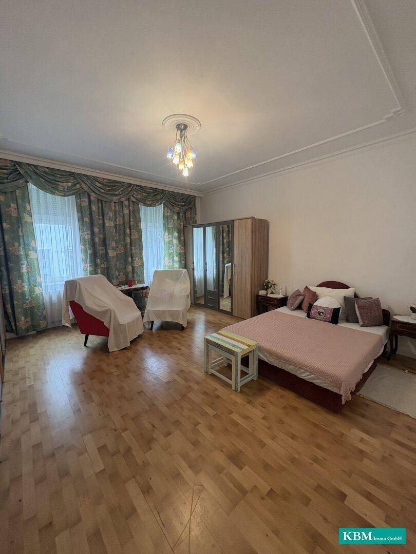 Geräumiges Schlafzimmer mit Holzboden, floralen Vorhängen und einem großen Kleiderschrank.