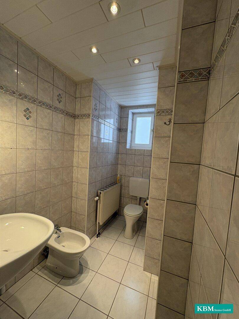 Gefliestes WC mit Bidet, Toilette und Fenster für natürliche Belüftung.