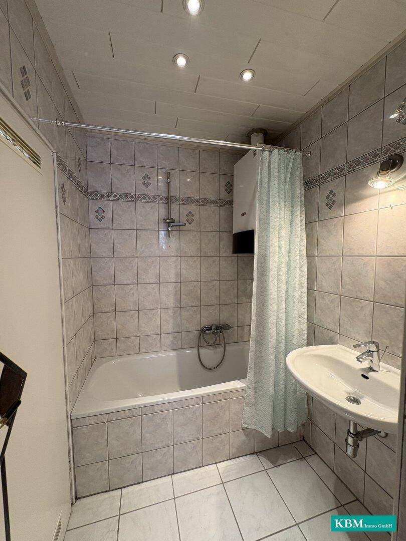Badezimmer mit Badewanne, Waschbecken und Fliesenboden in hellem Design.