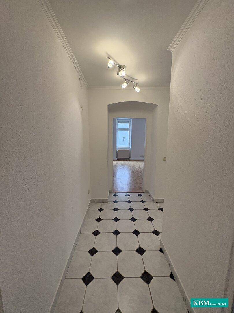Heller Flur mit schwarz-weißem Fliesenboden und Zugang zu weiteren Räumen.