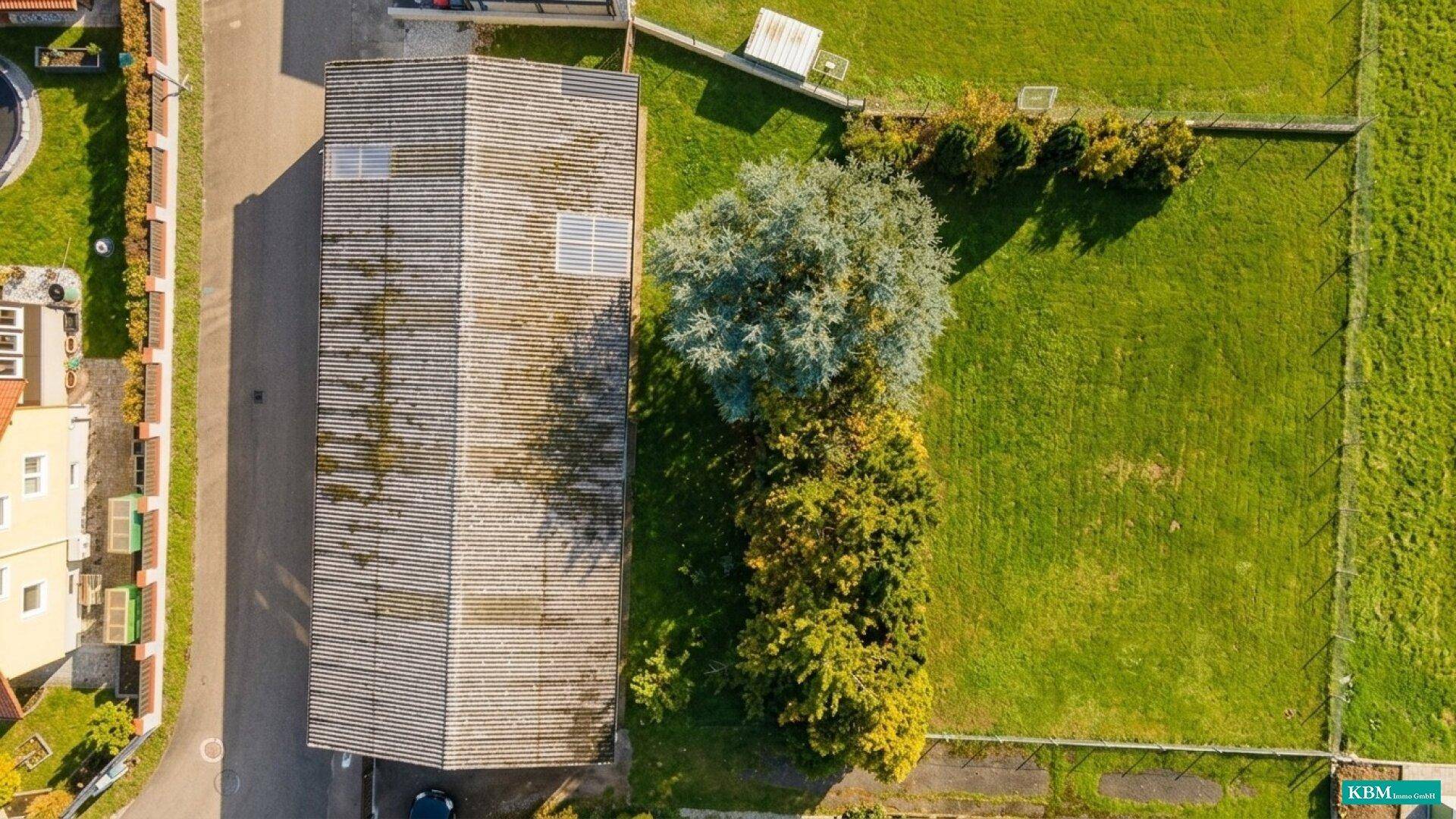 Senkrechte Luftaufnahme eines langen Gebäudes mit Satteldach und angrenzender großer Rasenfläche.