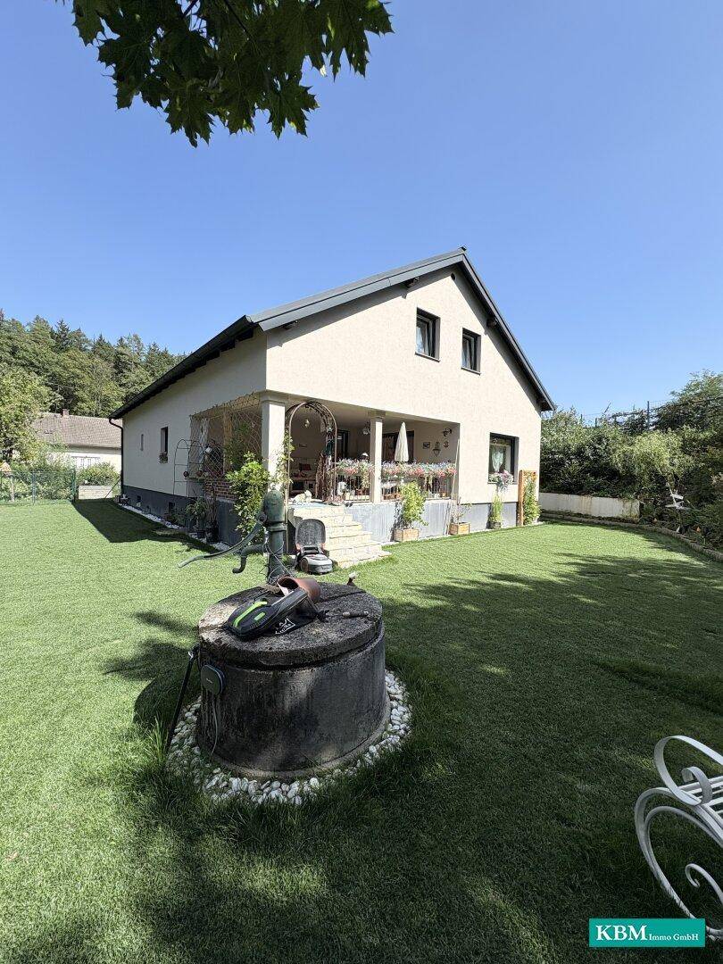 Freistehendes Haus mit großem Garten, Rasenfläche und einem alten Brunnen im Vordergrund.