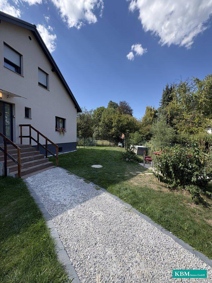Seitenansicht des Hauses mit Kiesweg zum Eingang und gepflegtem Gartenbereich.