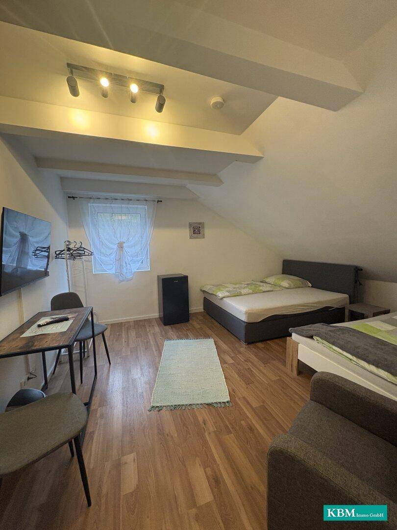 Schlafzimmer mit zwei Betten, kleinem Kühlschrank und Fernseher, beleuchtet durch ein Fenster.