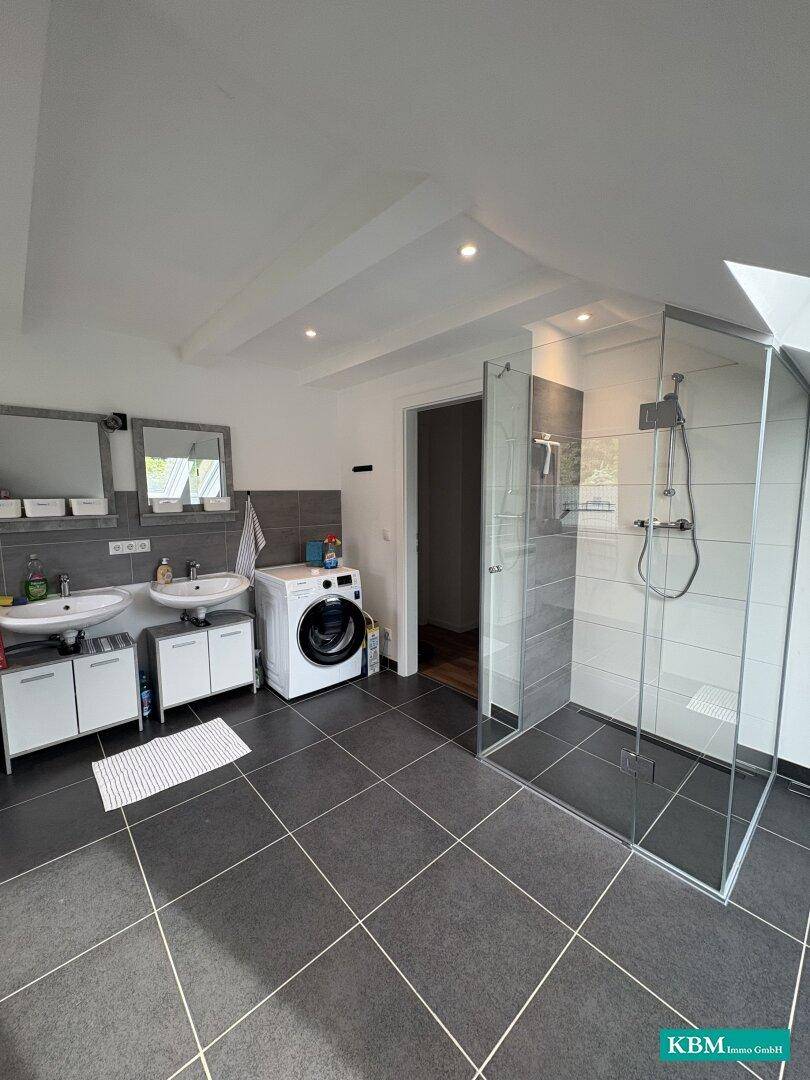 Modernes Badezimmer mit begehbarer Dusche, Doppelwaschbecken und Waschmaschine unter Dachschräge.