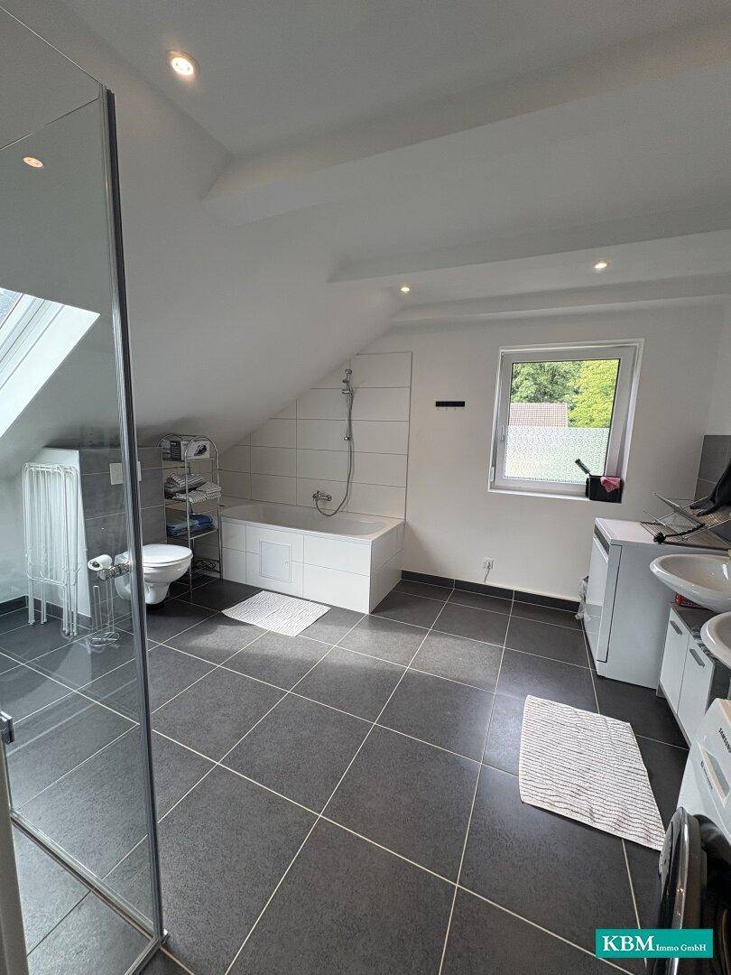Geräumiges Badezimmer mit Badewanne, Dusche, WC und Doppelwaschbecken unter Dachschräge.
