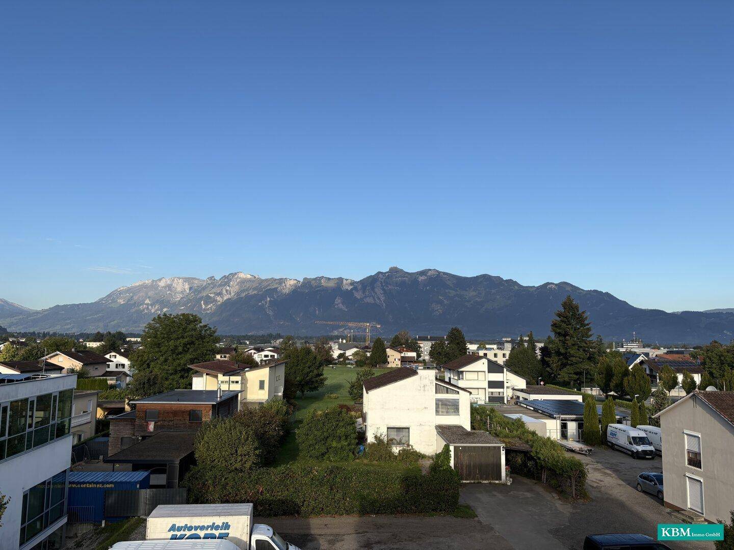 Weitläufige Aussicht über eine Siedlung mit Bergen im Hintergrund unter klarem blauem Himmel.