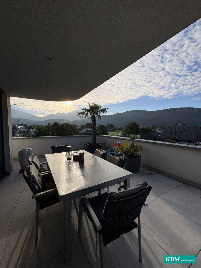 Möblierte Terrasse mit Esstisch und Stühlen, umgeben von Pflanzen und einem weiten Bergblick.