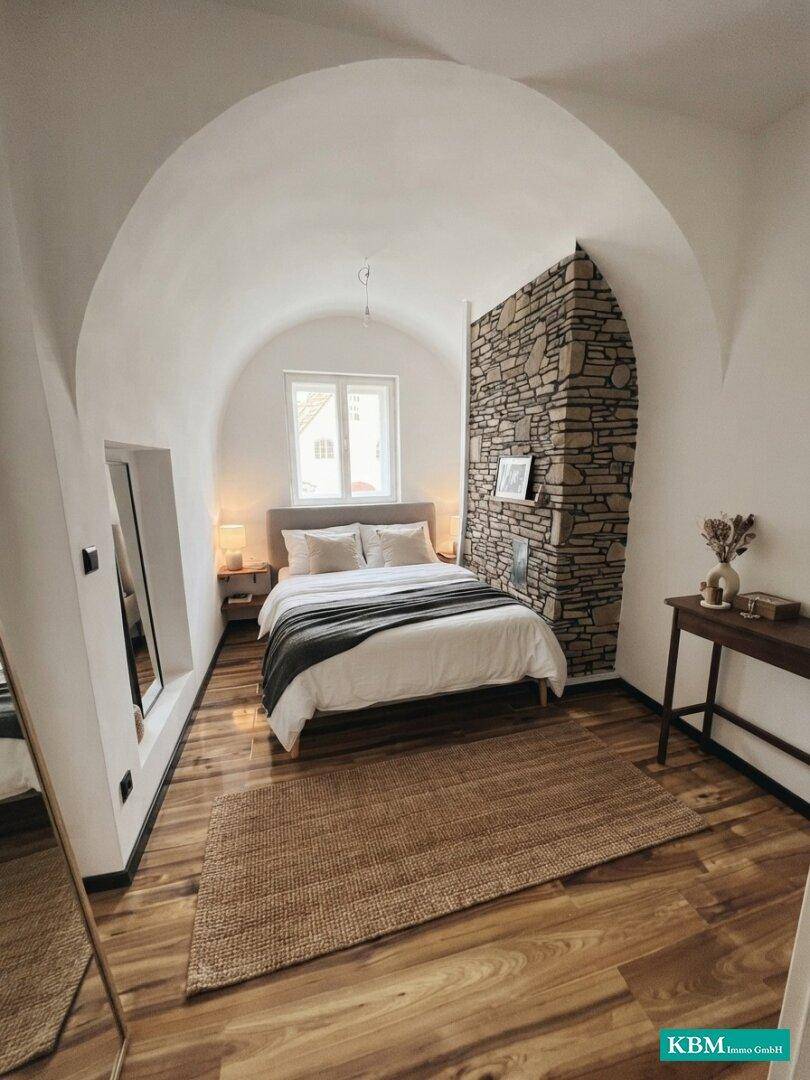Gemütliches Schlafzimmer mit Gewölbedecke, Holzboden und dekorativer Steinwand, die Charakter verleiht.