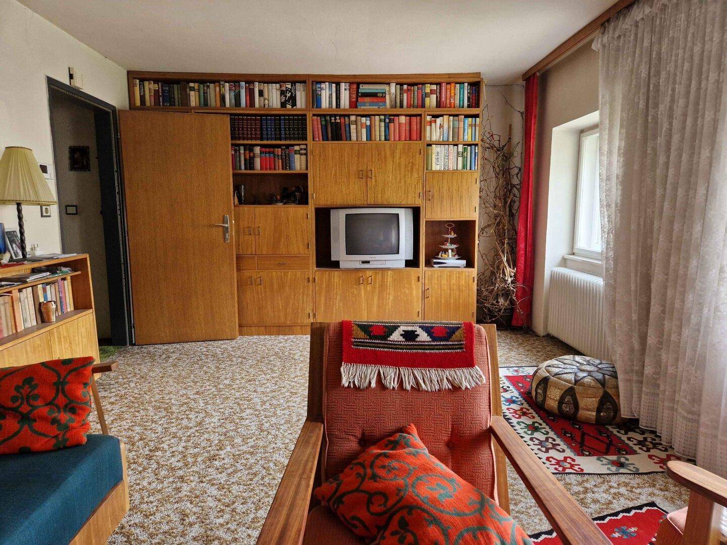Wohnzimmer mit großer Bücherwand, Fernseher und bequemen Sesseln, das eine wohnliche Atmosphäre bietet.