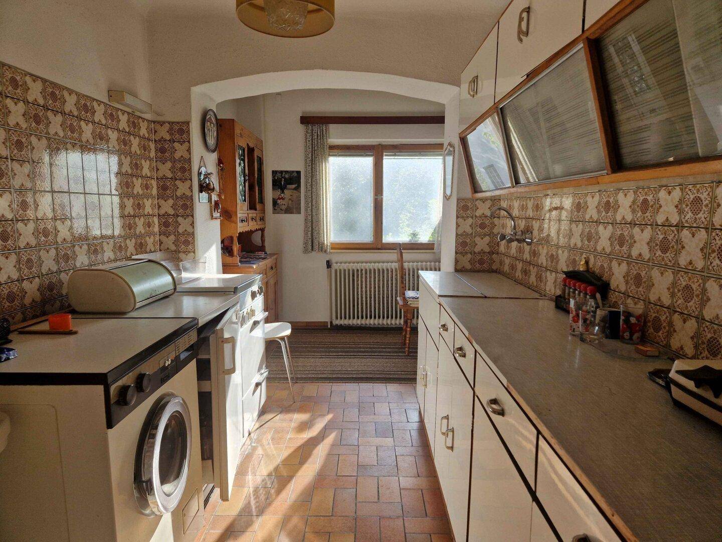 Funktionale Küche im Retro-Stil mit gemusterten Fliesen, Spüle und Waschmaschine, die viel Tageslicht erhält.