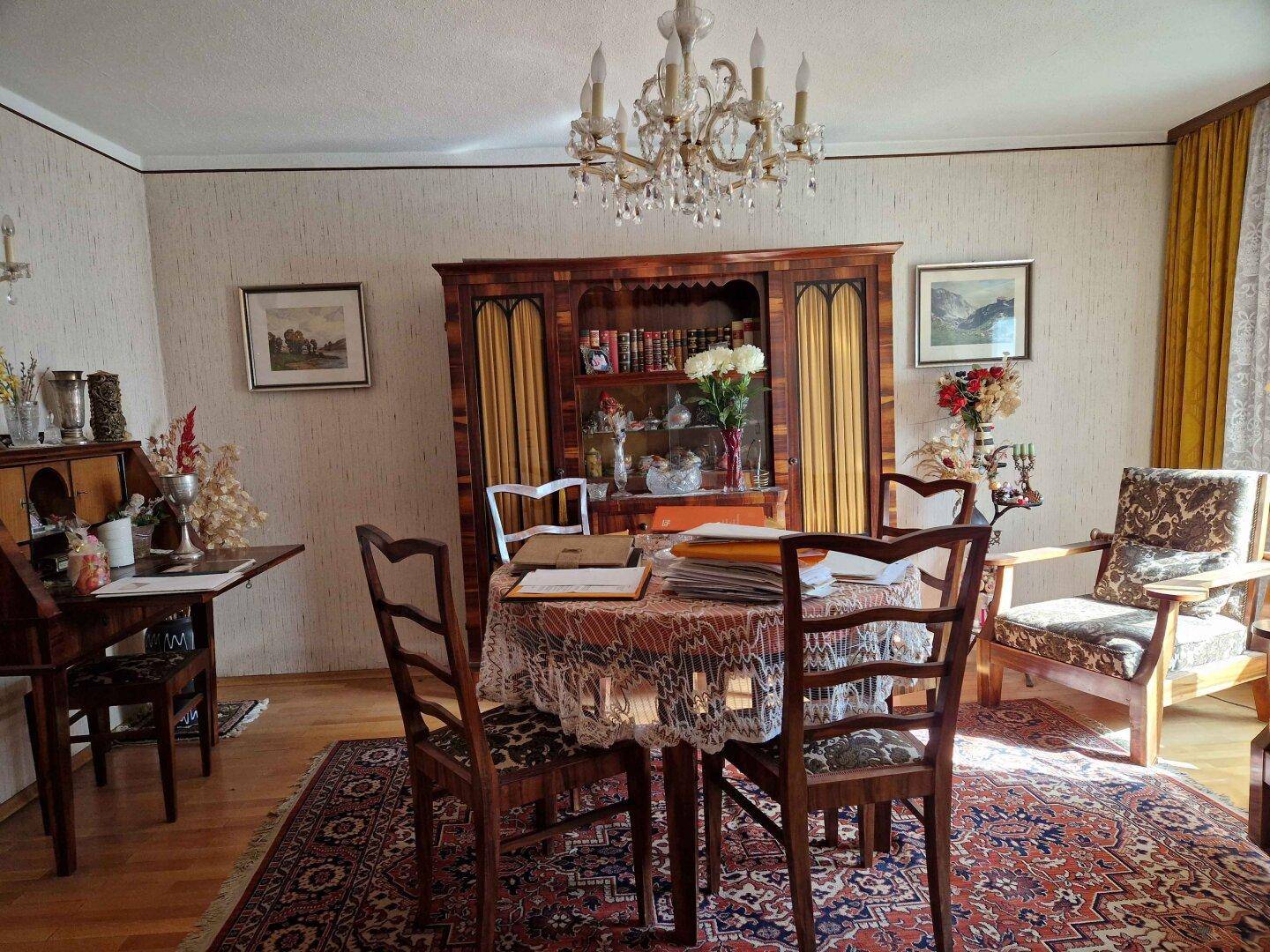 Gemütlicher Essbereich mit klassischem Holztisch, Stühlen und einem großen Schrank, beleuchtet von einem Kronleuchter.