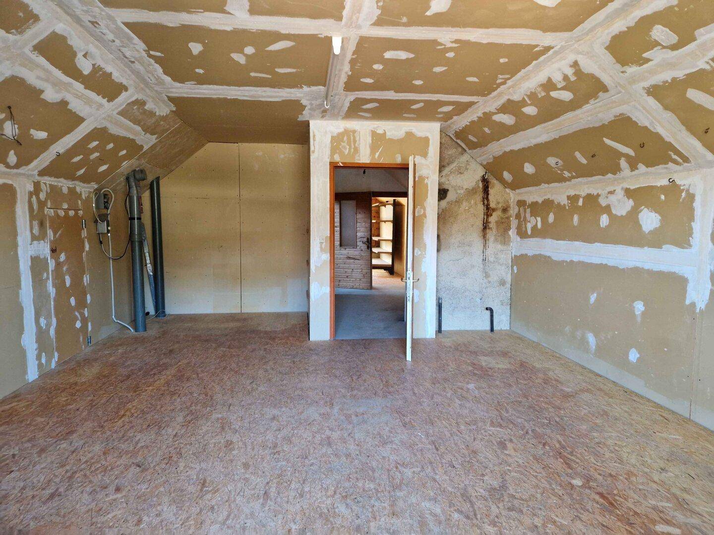 Unausgebauter Dachbodenraum mit Dachschrägen, sichtbaren Trockenbauplatten und Holzspanplattenboden.