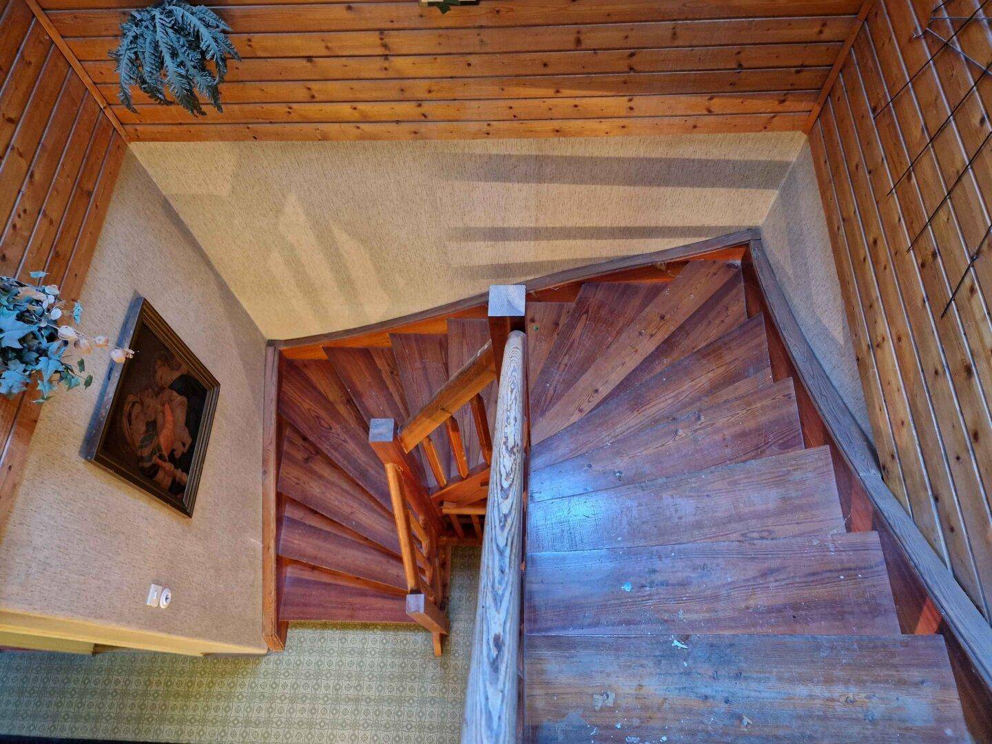 Blick von oben auf eine geschwungene Holztreppe mit Holzgeländer und traditioneller Dekoration.