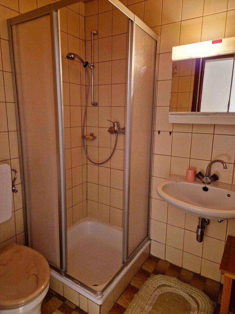 Kleines Badezimmer mit Duschkabine, WC und Waschbecken in beigen Fliesen.