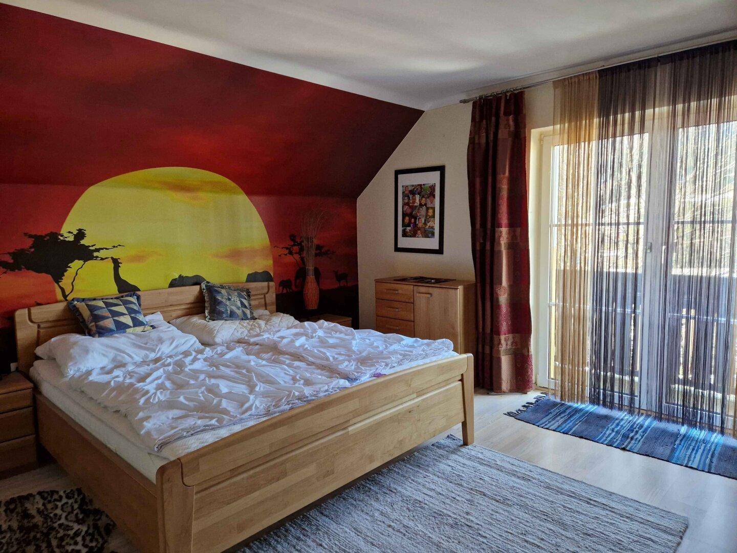 Schlafzimmer mit Doppelbett, Balkonzugang und Wandgemälde im Sonnenuntergang-Stil.