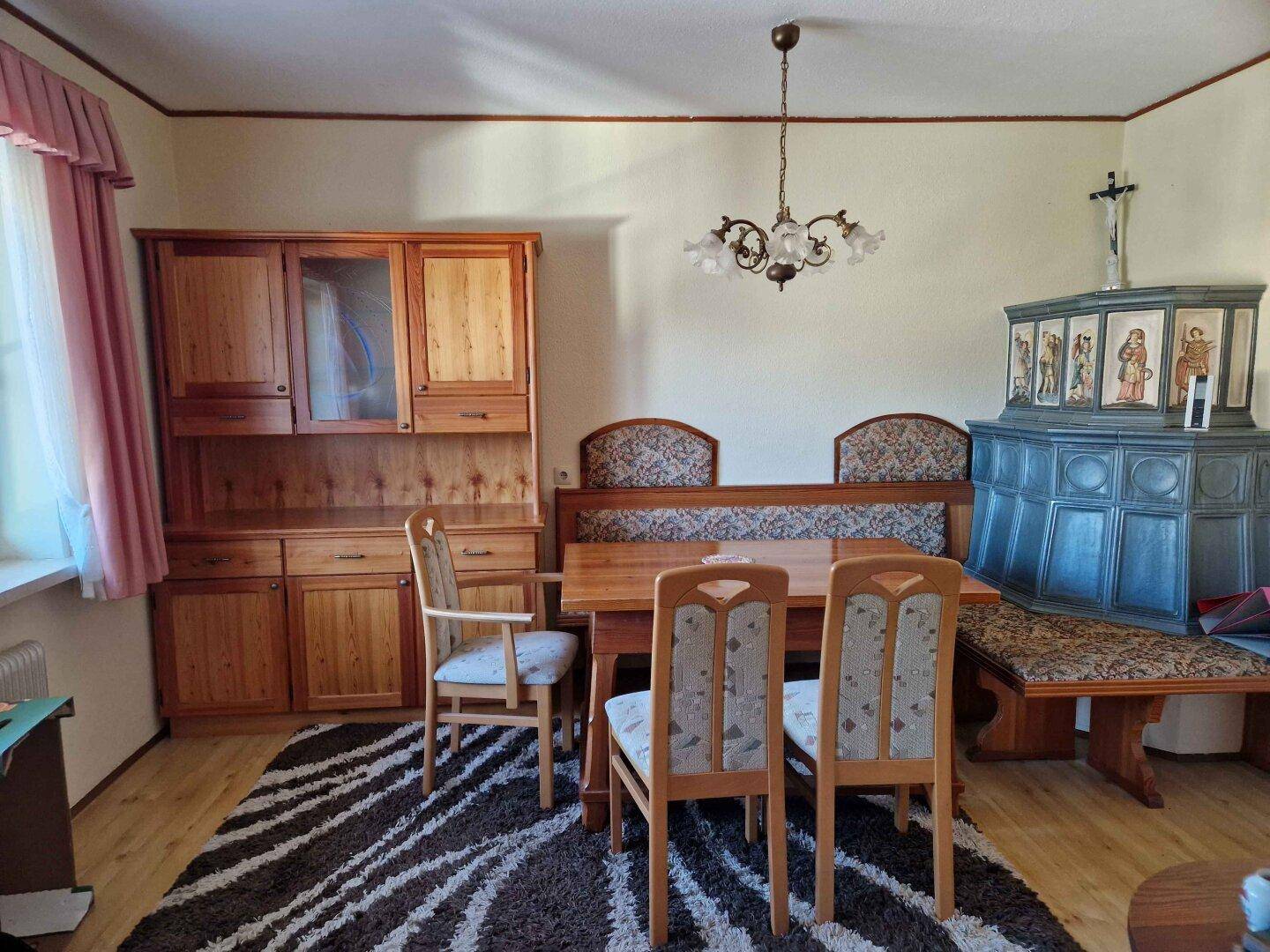 Gemütlicher Essbereich mit Holztisch, Eckbank und traditionellem Kachelofen.